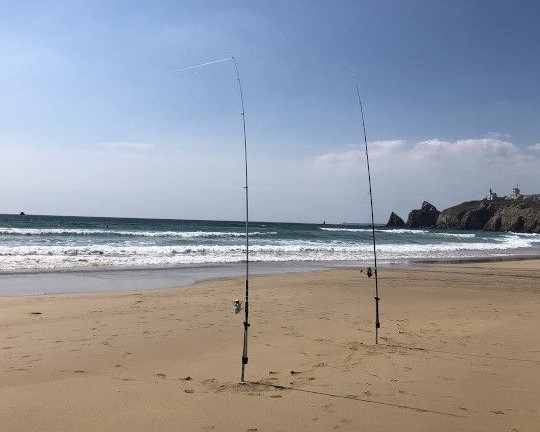 Deux cannes de surfcasting en action de pêche dans une mer agitée par des rouleaux.